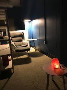 Corner of the quiet room with reading chair, illuminated by soft lighting form a floor lamp and a salt lamp. 