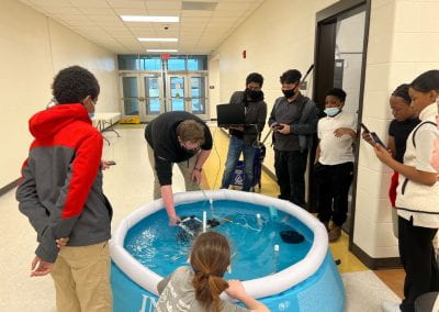 Students surrounding Filled pool watching a STEMBot driving